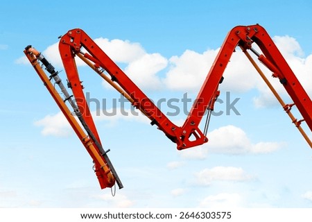 Construction machine mobile concrete pump with red extended boom arms against blue sky and  clouds preparing for pour