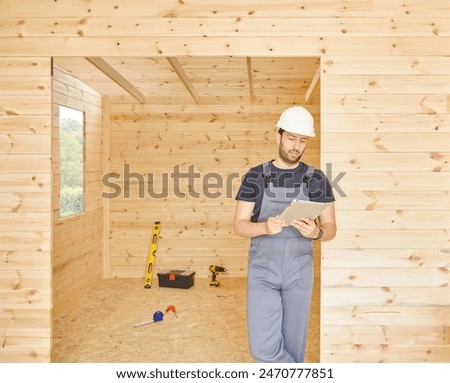 Construction man, builder man construct new wooden home, tiny house style. Spirit level, screw, tool bag and charged drill. Wood shelter style.