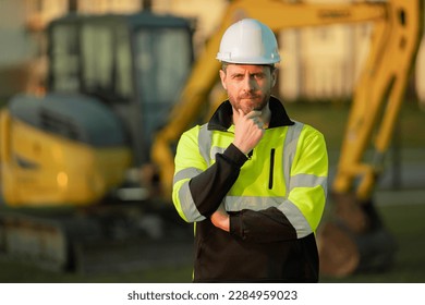 Construction man with excavator at industrial site. Worker in helmet build with bulldozer. Engineer work with builder contractor in hardhat. Excavation foreman with tractor. Workman with excavator.