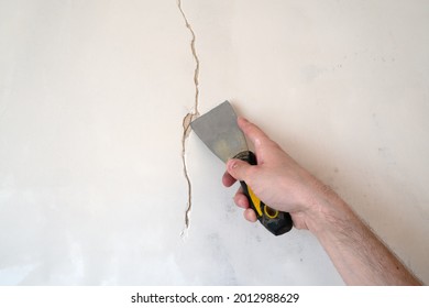 Construction Man Worker Repairing A Crack Wall Of A Home, Plastering Cement On Wall. Builder Applying White Cement To A Crack In A Wall With A Putty Knife. Close Up 