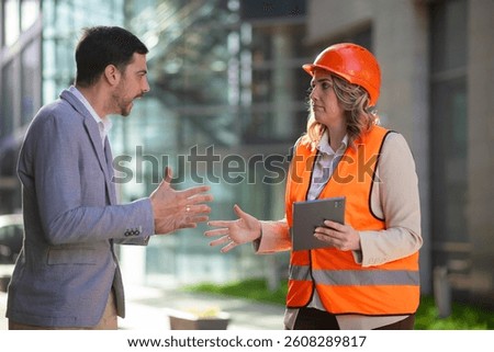 Construction manager and engineer discussing a problem at the building site. Female professional looks confused while checking information on a tablet.