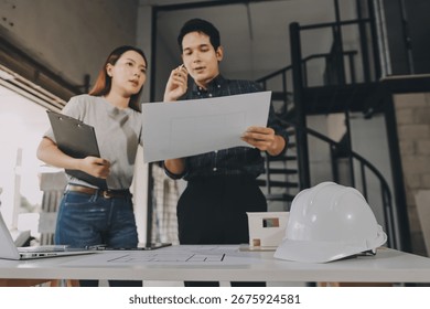 Construction manager and engineer dressed in orange work vests and hard helmets explore construction documentation on the building site near the steel frames
