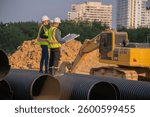 Construction Manager and engineer working construction site blueprint for survey inspection detail of construction with pipe heavy machinery excavator constructed hi-way road background.