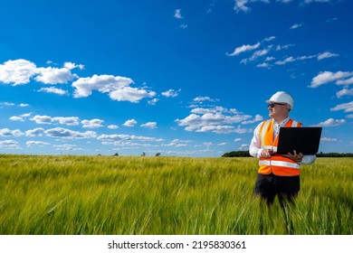 Construction Manager With Laptop. Man In Builder Helmet. Construction Team Manager In Middle Of Wheat Field. Construction Company Manager Inspects Land. Site Selection For Building Concept