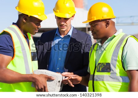 construction manager and two workers examining a brick