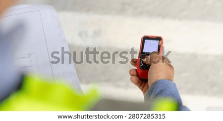 Construction manager utilizing a mobile device to oversee project management on site while holding blueprints