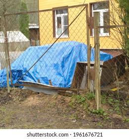 Construction Materials Covered With Foil In A Messy Yard Behind Fence