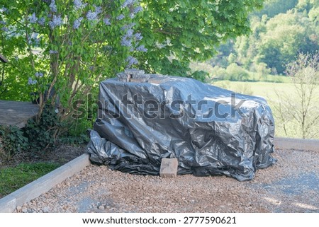 Construction materials covered with a protective tarp outdoors. The cover shields equipment from weather conditions such as rain, dust, and sunlight.