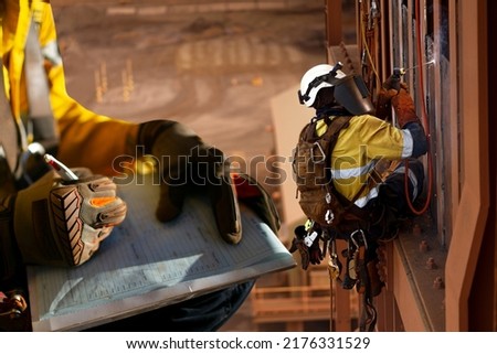 Construction miner supervisor wearing safety glove signing working at height working permit on open field job site prior to starting high risk rope access working at height construction mine site 