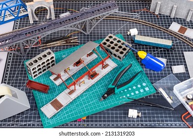 Construction Of A Model Railroad Layout. Workbench With Model Railway Train Station Bridge Tracks And Landscape Tools. Hobby Leisure Scale Modelling Concept