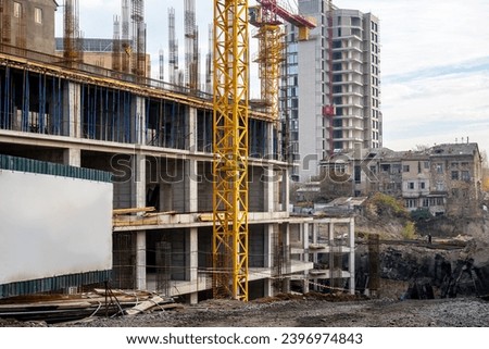 Construction of multi-storey building. Tower crane is constructing stone building. Construction site without workers. Erection of monolithic buildings. Residential area under construction