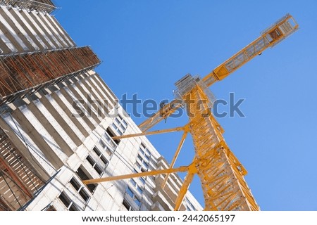 Construction of a multi-storey building using a high-rise yellow crane. Home construction. Crane and building under construction against blue sky. Construction work site.