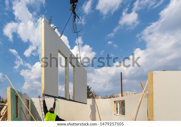 Construction new and modern modular house from\
composite sip panels. Worker man in uniform wear working on\
building development industry of energy efficient property against\
blue sky\
background