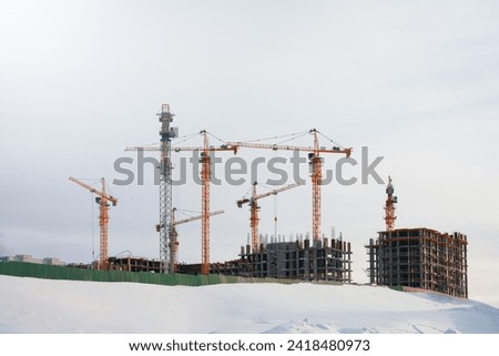 Construction of a new neighborhood. Winter. Panoramic view of a snow-covered construction site with many construction cranes against the cold sky. Copy space.                               