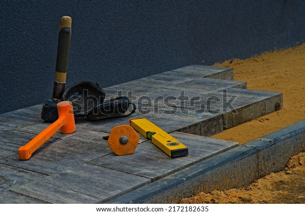 Construction of a new tiny pavement (band) of concrete\
paving stones. Paving tools like: orange hammer inertia , a rubber\
hammer, protective knee pads, a chisel and a spirit laser level\
.