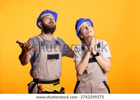 Construction partners glance upward with dramatic frustration, facing renovation setbacks. Renovators pleading for good news during unpredictable challenges of building, repairs and DIY projects.