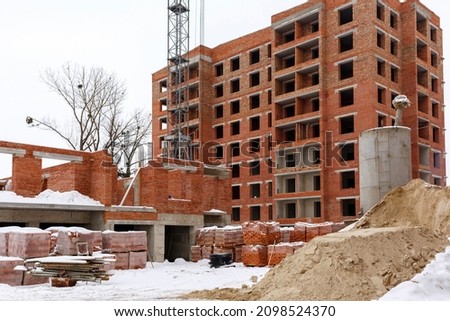 Construction process of brick buildings, brick walls, concrete foundation, building materials, sand, brick pallets. Unfinished construction buildings.