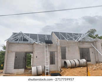 Construction process of a single-story residential house using lightweight concrete blocks (AAC) and light steel roof trusses under a cloudy sky.
