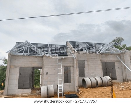 Construction process of a single-story residential house using lightweight concrete blocks (AAC) and light steel roof trusses under a cloudy sky.