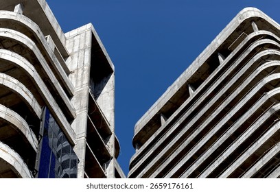 Construction process of skyscraper. Exposed concrete framework with geometric facade, raw structure in blue sky, modern highrise apartment and office tower, urban housing development project.