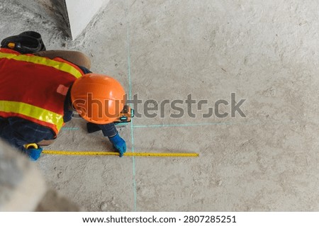 Construction professional using a laser leveling tool to accurately measure the floor layout at a busy job site