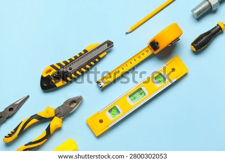 Construction and renovation tools flat lay with utility knife measuring tape level pliers and screwdriver on blue background