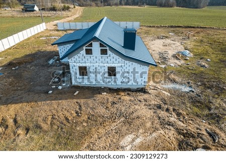 Construction and repair of country houses. New cottage with double-glazed windows on the plot. Aerial view from a drone to a construction site in a field. Construction of social housing.