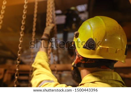 Construction rigger high risk worker crane operator wearing fall protection safety helmet holding chains on chain block while defocused friend at the background    