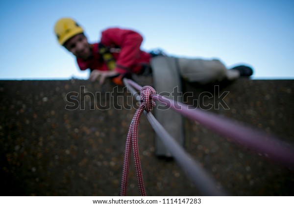 Construction rope access worker climbing up over the\
edge using, fasten Alpine Butterfly knot to isolated damage, cut of\
rope for safety precaution in high rise building, Sydney city,\
Australia    