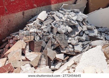 Construction rubble and broken tiles in dumpster. Renovation debris waste pile scene. Demolition materials disposal concept. Building trash container closeup. Industrial cleanup texture.
