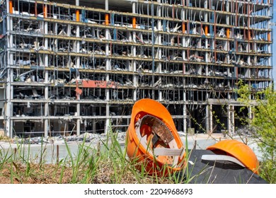
Construction safety helmets are in foreground against background of residential or office building under construction or damaged by explosion of ammunition or military missile. House reconstruction