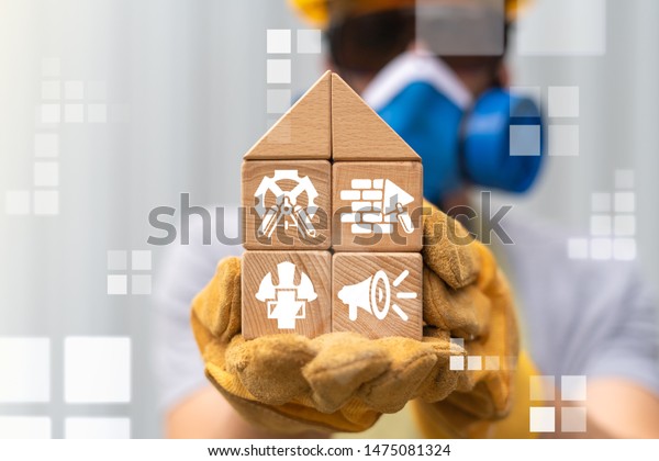 Construction\
Safety Industry concept. Safe Build. BIM building information\
modeling safety work concept. Worker in safety gear holding wooden\
block house model with construction\
icons.