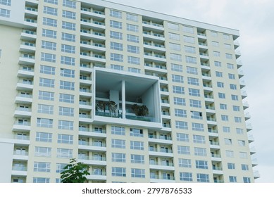 Construction shows a modern building with multiple floors and many windows. A large balcony extends out from the facade. Trees are visible on the balcony, creating an urban garden feel.