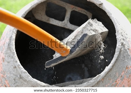 Construction site. Adding lime, sand and stones to rotating cement mixer. Builder working with shovel during concrete solution mortar preparation. Bricklayer job machine equipment. Cement slurry