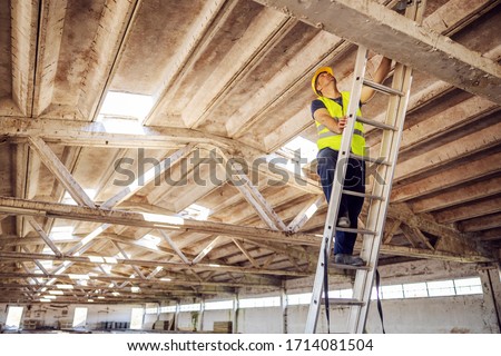 Construction site builder climbing on ladder and preparing to fix rooftop.