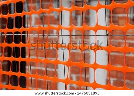 Construction site for a building surrounded by an orange protective fence to prevent unauthorized access to work area