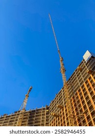 Construction site with a building under construction, dominated by a large yellow crane Exposed steel beams and rebar suggest ongoing work or reinforcement Smaller structures might be temporary pla