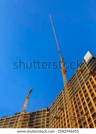 Construction site with a building under construction, dominated by a large yellow crane Exposed steel beams and rebar suggest ongoing work or reinforcement Smaller structures might be temporary pla