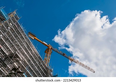 Construction Site In A City With Tall Crane Against Blue Cloudy Sky. Frame Of The Building Is In Scaffolding Without Safety Net. New Residential And Commercial Property Development.