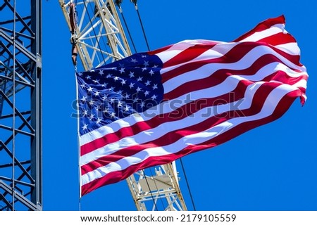 A construction site crane flying a United States Flag with a clear blue sky on a bright sunny day