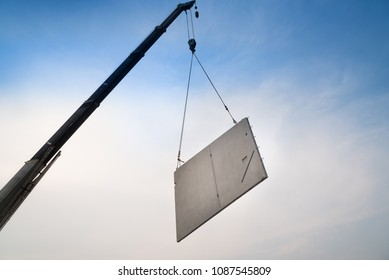Construction site crane is lifting a precast concrete wall panel to installation building.