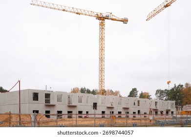 construction site with cranes and building in progress. large cranes tower over partially built concrete structure against cloudy sky, signifying urban development, progress, and industry