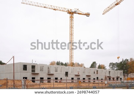 construction site with cranes and building in progress. large cranes tower over partially built concrete structure against cloudy sky, signifying urban development, progress, and industry