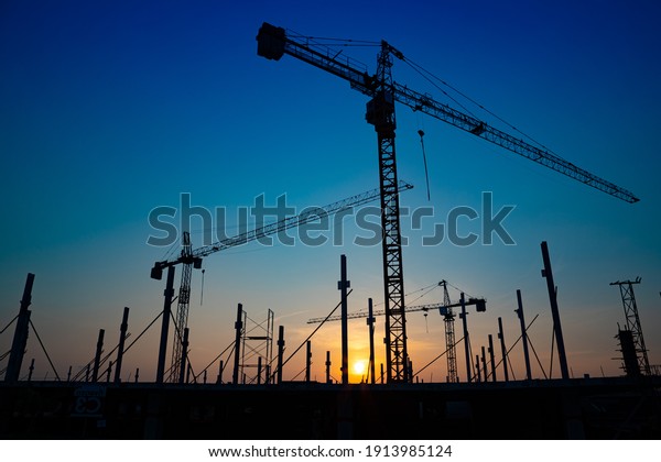 Construction\
site with cranes on orange sunset, sunrise sky background. Steel\
frame structure, structural steel beam build large buildings at\
construction site . construction\
machinery.