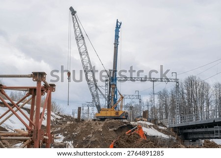 Construction site with crawler crane and piling rig machine. Worker standing near heavy industrial equipment for bridge repair. Infrastructure development and civil engineering project.