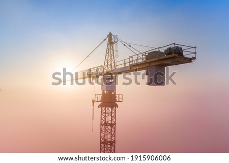 Construction site at dawn. Tower cranes over fog on the background of the morning sun. Drone view