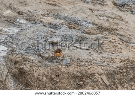 Construction site in disarray, featuring demolition debris, uneven terrain, rusted metal bucket, wooden plank, sparse vegetation, natural lighting, earth tones