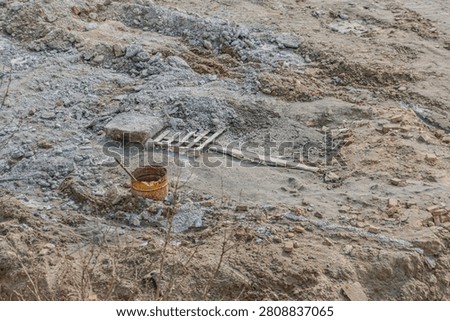 Construction site in disarray, showcasing uneven ground covered with dirt and rocks, featuring scattered materials like rusted bucket, wooden pallet, weathered plank, emphasizing work-in-progress