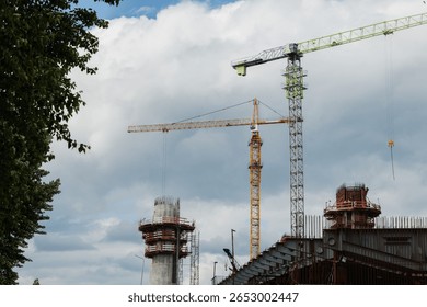 Construction site features multiple cranes and scaffolding under a dramatic cloudy sky, highlighting urban development and engineering progress