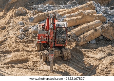 Construction site featuring earth moving vehicle, muddy terrain, piles of dirt and rocks, concrete structures, early stage construction, sunny day lighting, sharp shadows, industrious activity